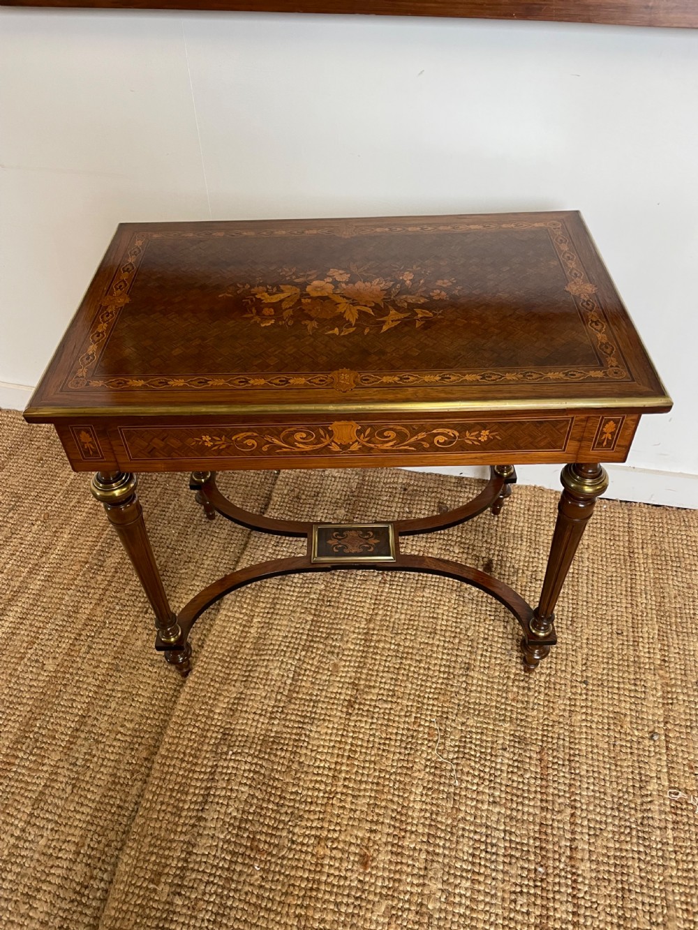 An overhead view of a French Napoleon III wooden side table featuring intricate floral marquetry on the top, slender turned legs, and brass edging. View III