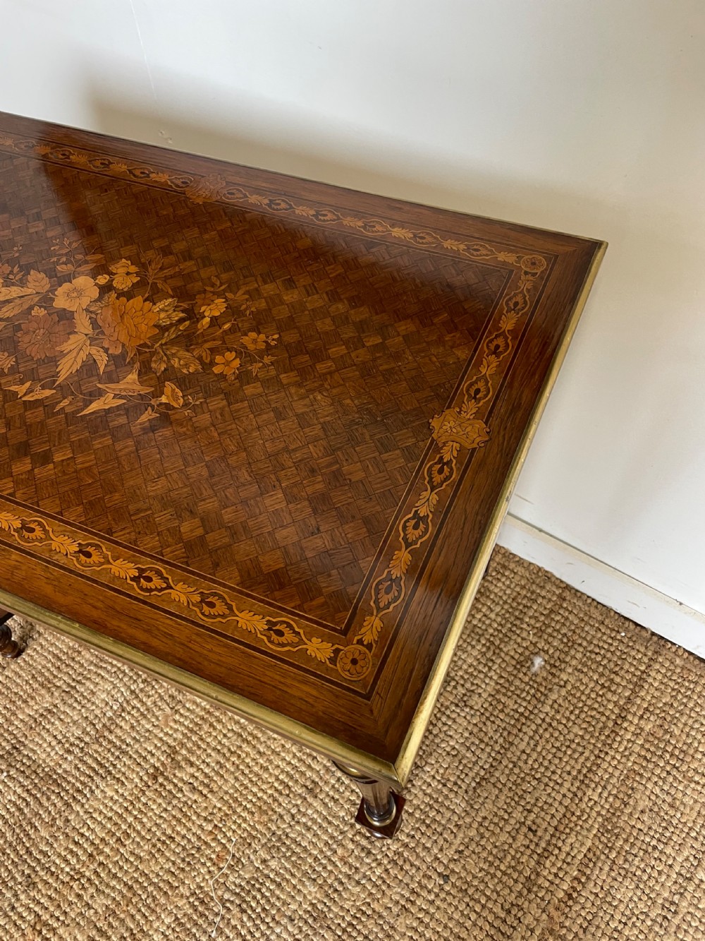 An overhead view of a French Napoleon III wooden side table featuring intricate floral marquetry on the top, slender turned legs, and brass edging. View V