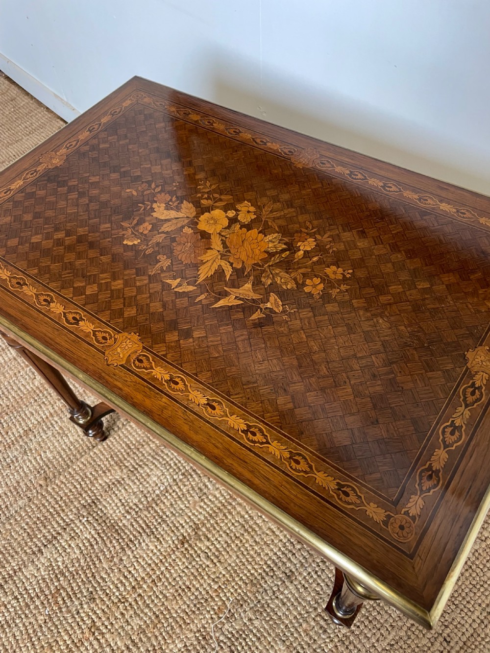 An overhead view of a French Napoleon III wooden side table featuring intricate floral marquetry on the top, slender turned legs, and brass edging. View VI
