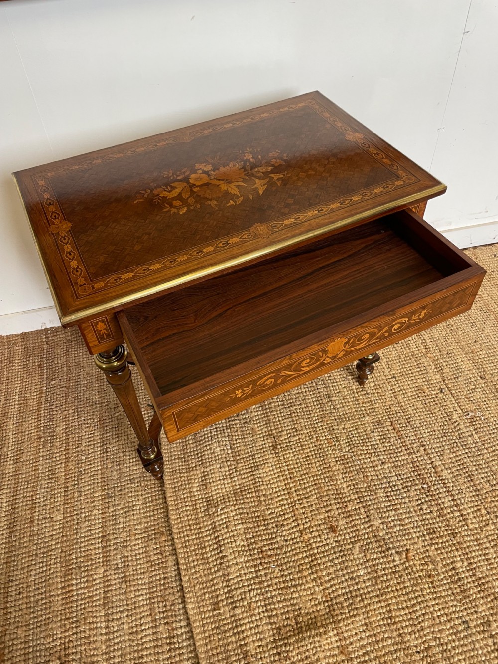 An overhead view of a French Napoleon III wooden side table featuring intricate floral marquetry on the top, slender turned legs, and brass edging. View IX