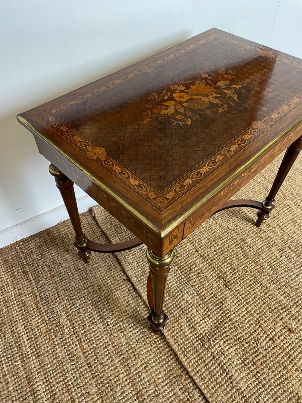An overhead view of a French Napoleon III wooden side table featuring intricate floral marquetry on the top, slender turned legs, and brass edging. View X