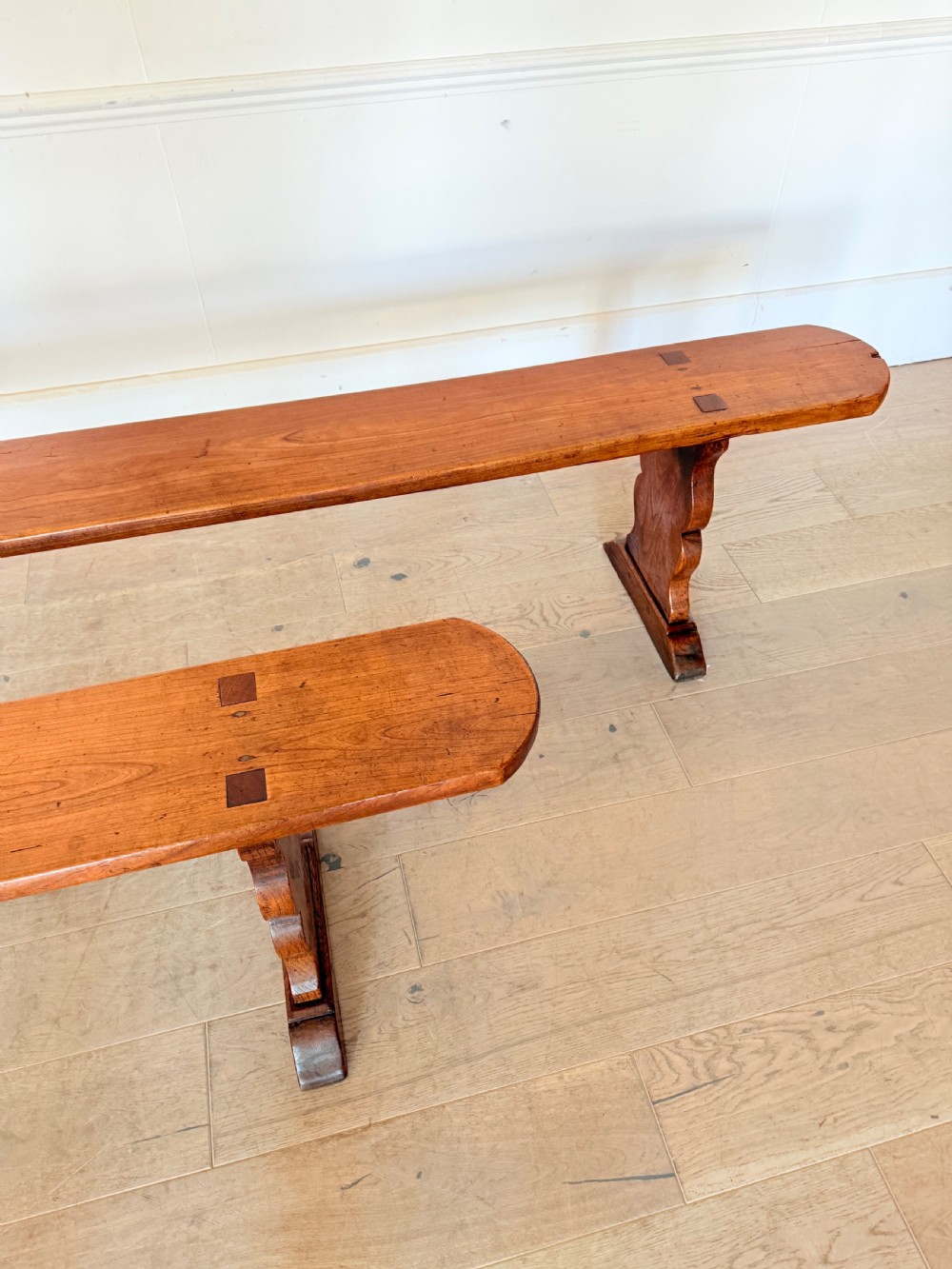 A pair of long 19th-century cherrywood benches with single-plank slab seats and shaped trestle end supports. View II