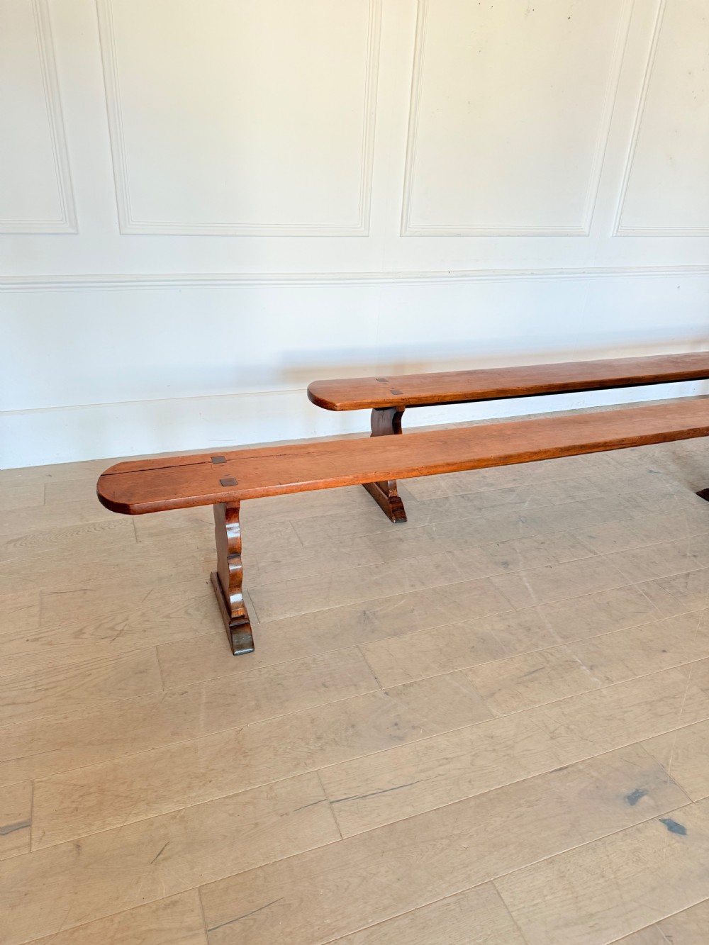 A pair of long 19th-century cherrywood benches with single-plank slab seats and shaped trestle end supports. View III