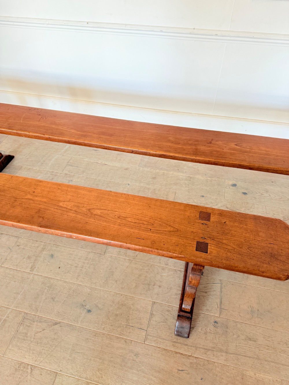 A pair of long 19th-century cherrywood benches with single-plank slab seats and shaped trestle end supports. View V