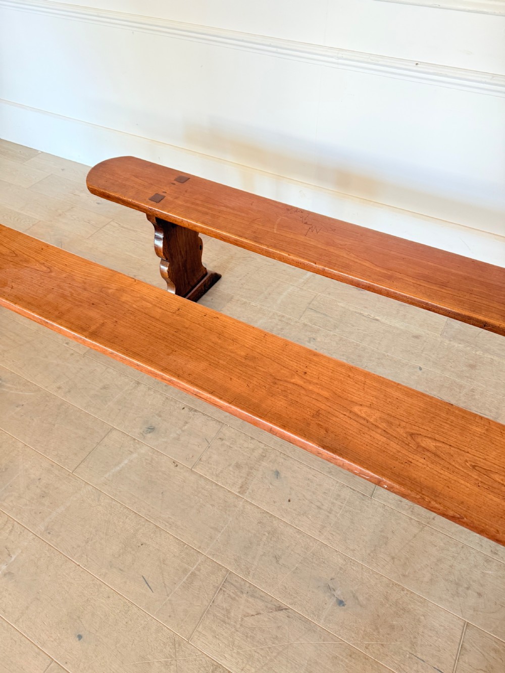 A pair of long 19th-century cherrywood benches with single-plank slab seats and shaped trestle end supports. View VI