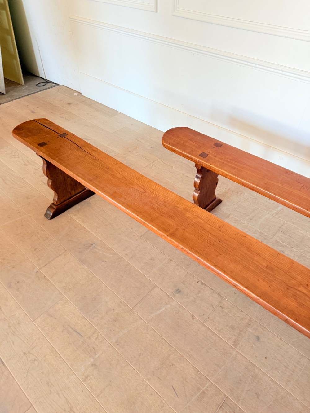 A pair of long 19th-century cherrywood benches with single-plank slab seats and shaped trestle end supports. View VII