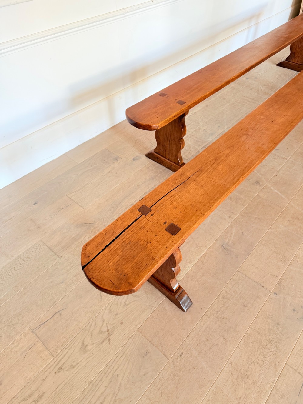 A pair of long 19th-century cherrywood benches with single-plank slab seats and shaped trestle end supports. View VIII