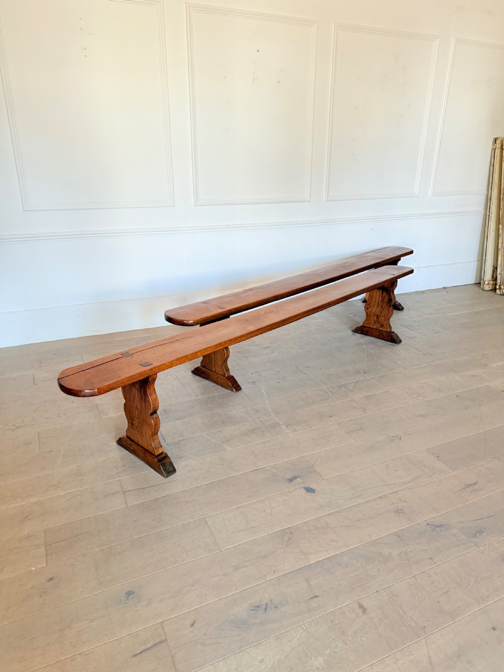 A pair of long 19th-century cherrywood benches with single-plank slab seats and shaped trestle end supports. View IX