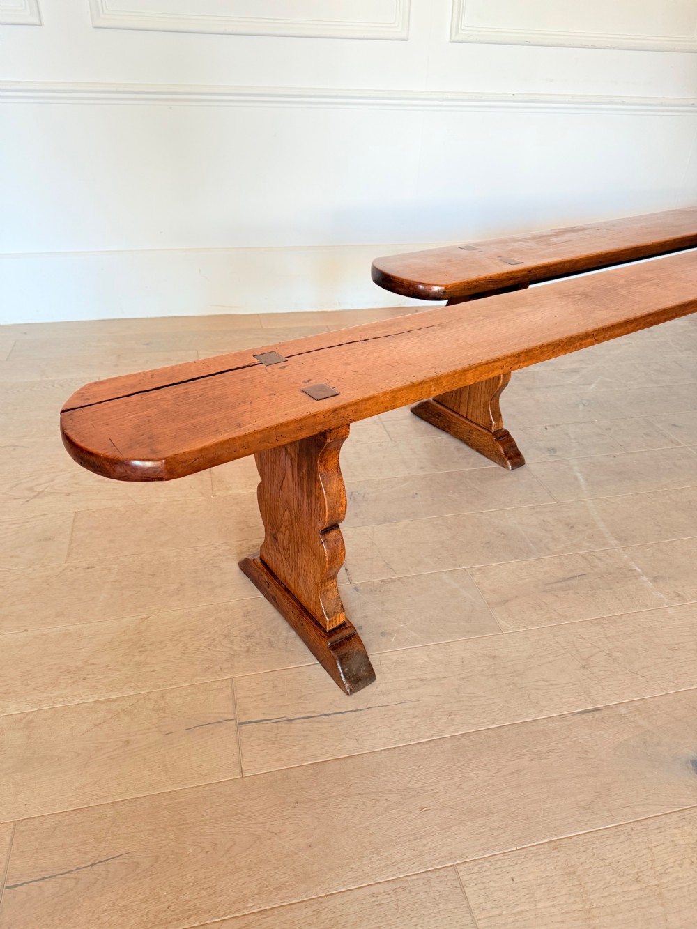 A pair of long 19th-century cherrywood benches with single-plank slab seats and shaped trestle end supports. View X