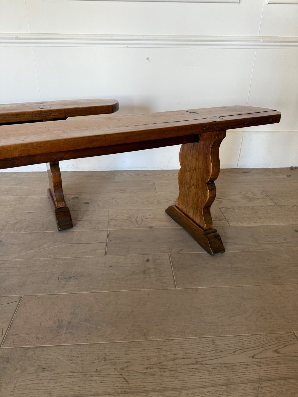 A pair of long 19th-century cherrywood benches with single-plank slab seats and shaped trestle end supports. View XI
