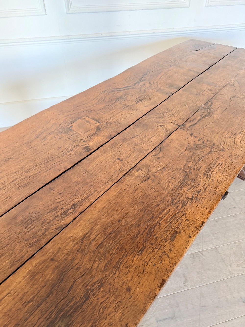 An early 19th century fruitwood refectory table featuring a plank top and trestle base against a white panelled wall. View VI