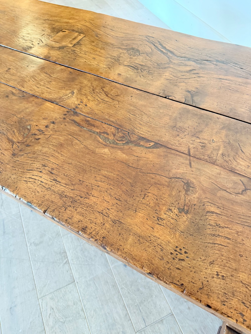 An early 19th century fruitwood refectory table featuring a plank top and trestle base against a white panelled wall. View XIII