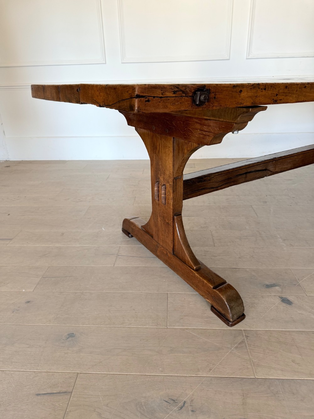 An early 19th century fruitwood refectory table featuring a plank top and trestle base against a white panelled wall. View XVI