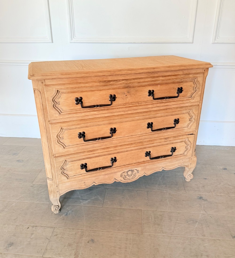 A scrubbed light oak commode chest featuring three long drawers with moulded panel detailing, iron drop handles, carved lower apron, and cabriole feet.