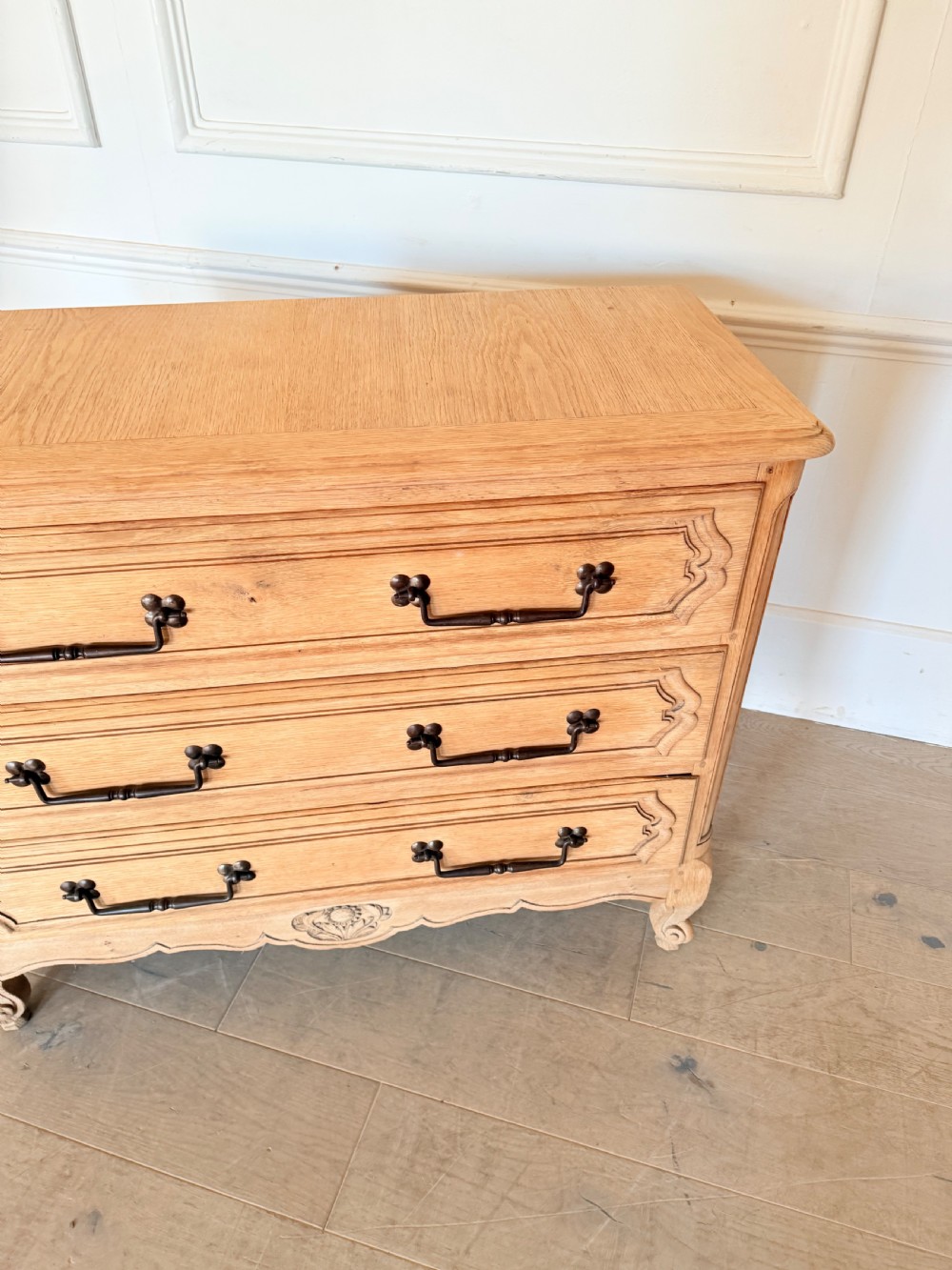 A scrubbed light oak commode chest featuring three long drawers with moulded panel detailing, iron drop handles, carved lower apron, and cabriole feet. View V
