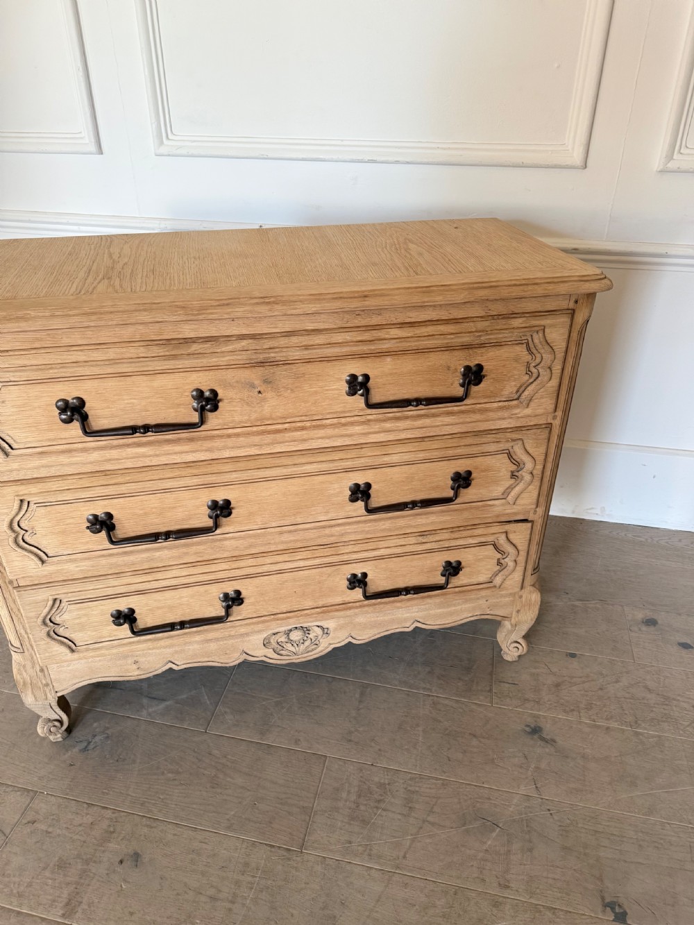 A scrubbed light oak commode chest featuring three long drawers with moulded panel detailing, iron drop handles, carved lower apron, and cabriole feet. View VI