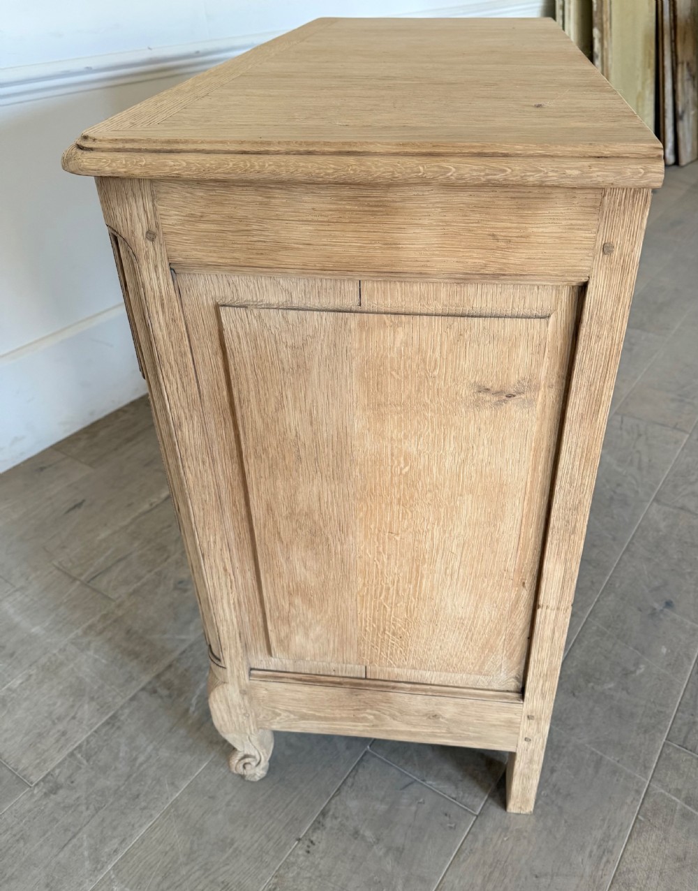 A scrubbed light oak commode chest featuring three long drawers with moulded panel detailing, iron drop handles, carved lower apron, and cabriole feet. View XI