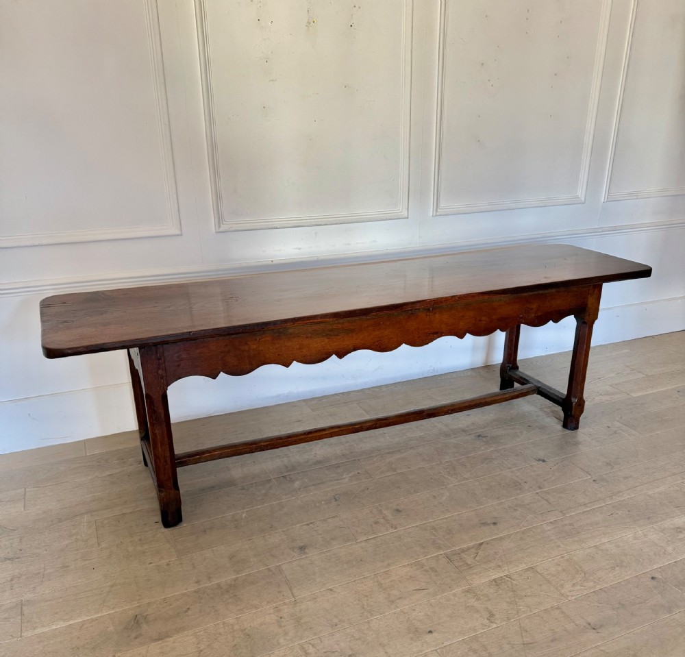 An eighteenth century oak console table with a rectangular plank top and a shaped frieze above plain stretcher-joined legs.