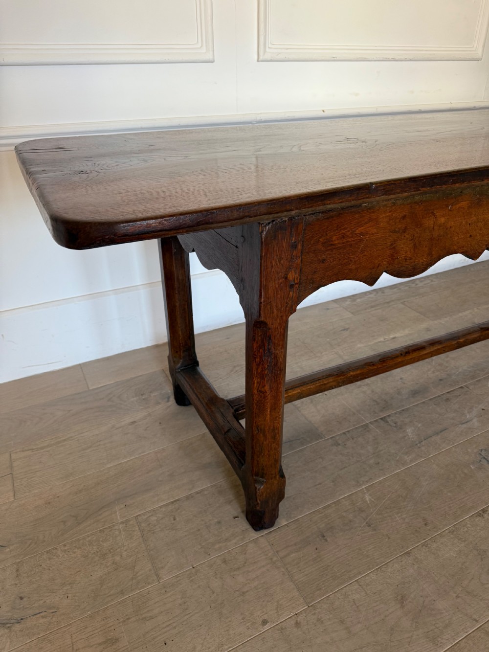 An eighteenth century oak console table with a rectangular plank top and a shaped frieze above plain stretcher-joined legs. View II