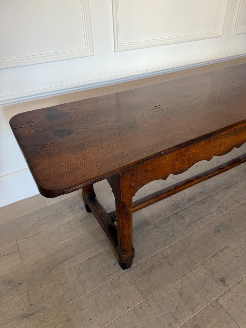 An eighteenth century oak console table with a rectangular plank top and a shaped frieze above plain stretcher-joined legs. View III