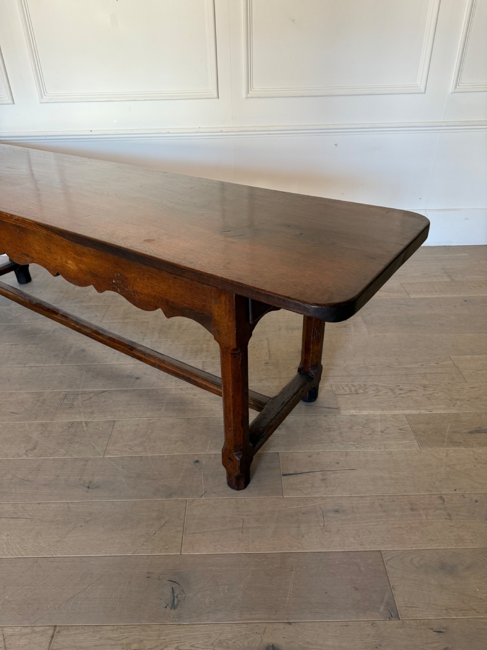 An eighteenth century oak console table with a rectangular plank top and a shaped frieze above plain stretcher-joined legs. View VII