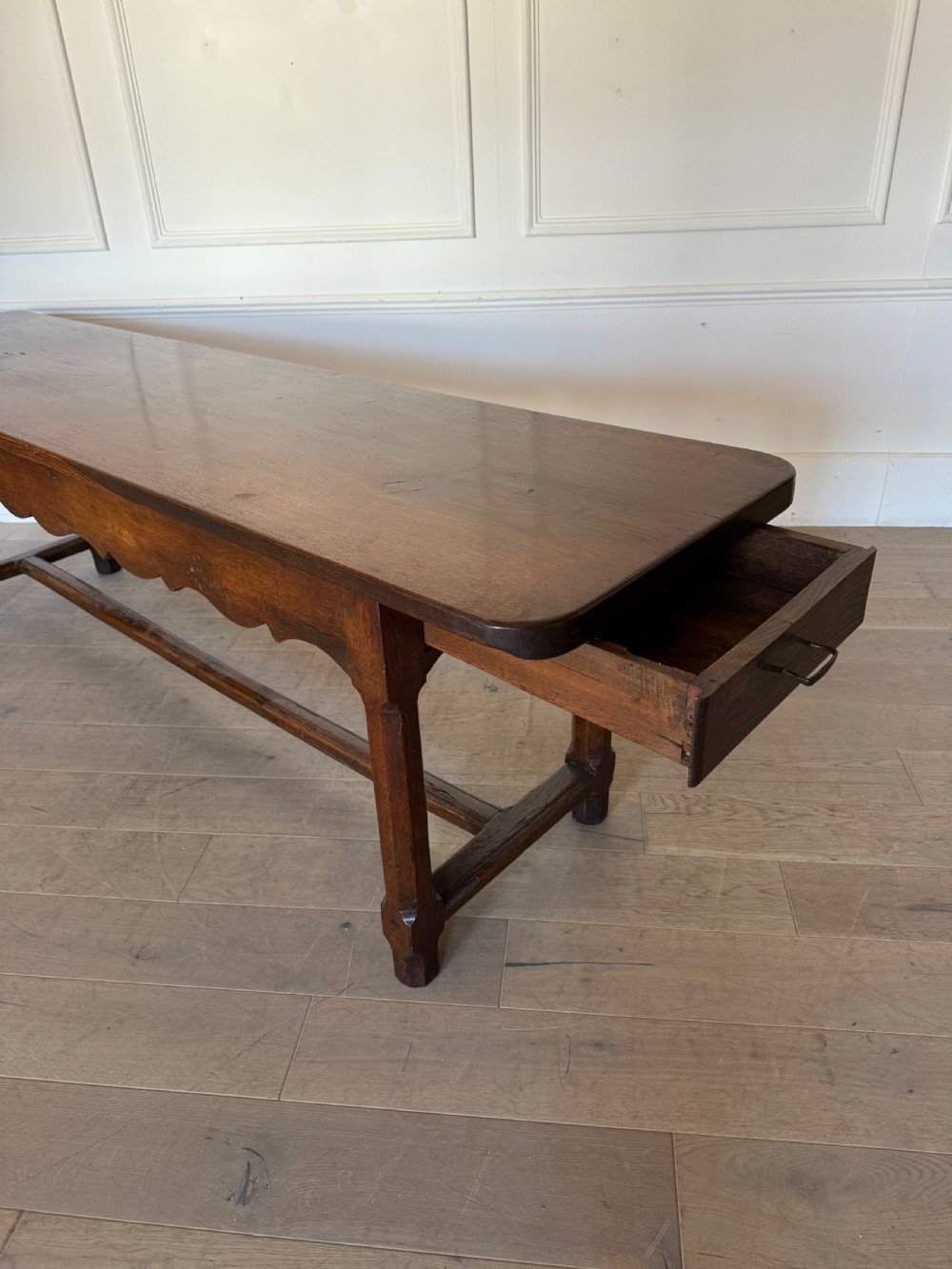 An eighteenth century oak console table with a rectangular plank top and a shaped frieze above plain stretcher-joined legs. View XII