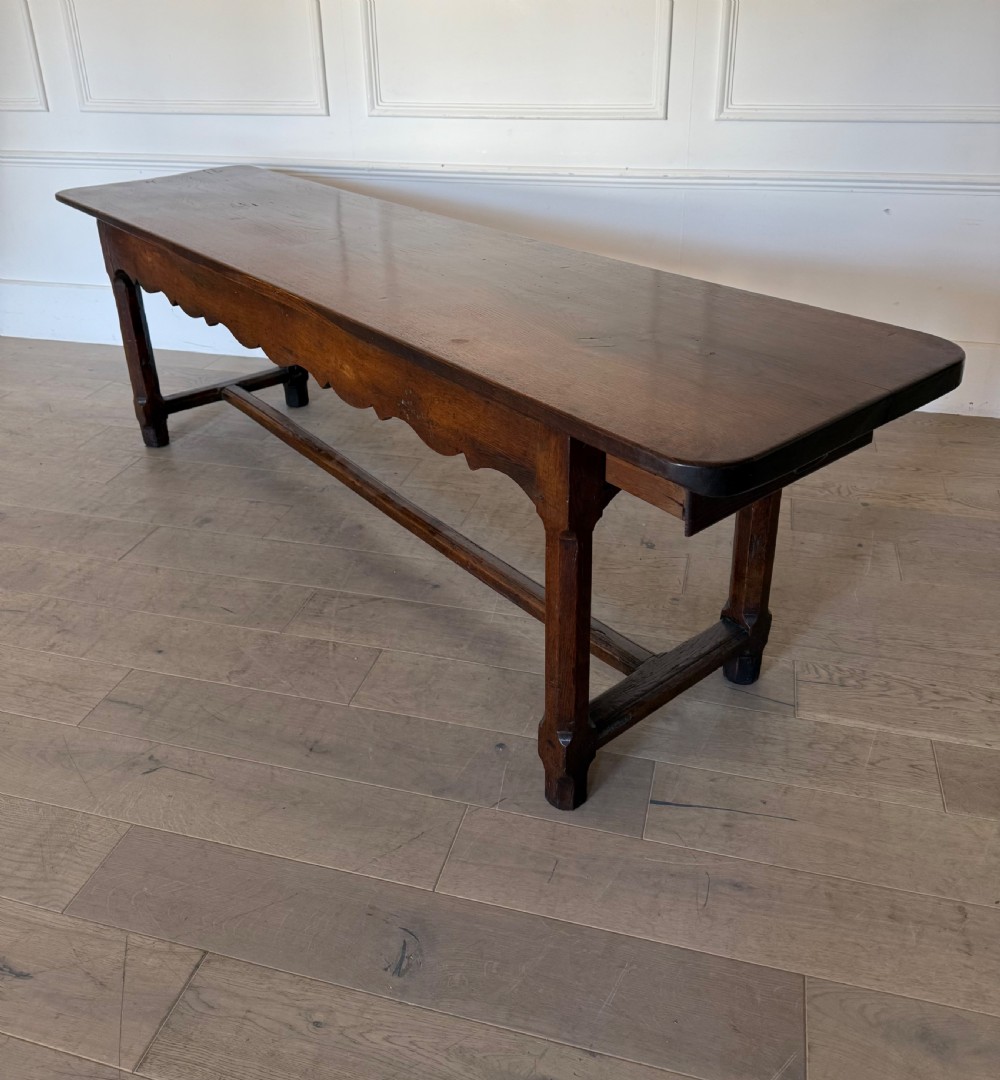 An eighteenth century oak console table with a rectangular plank top and a shaped frieze above plain stretcher-joined legs. View XIV