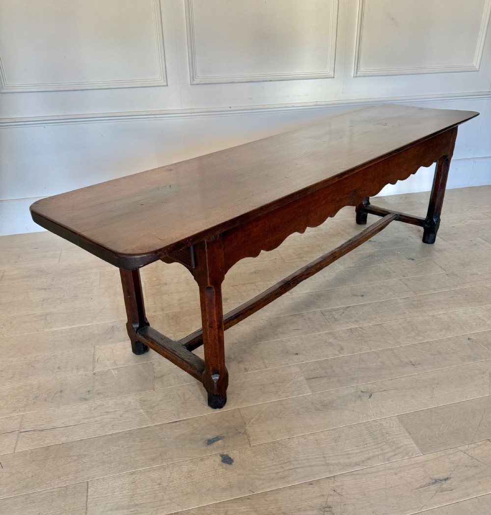 An eighteenth century oak console table with a rectangular plank top and a shaped frieze above plain stretcher-joined legs. View XV