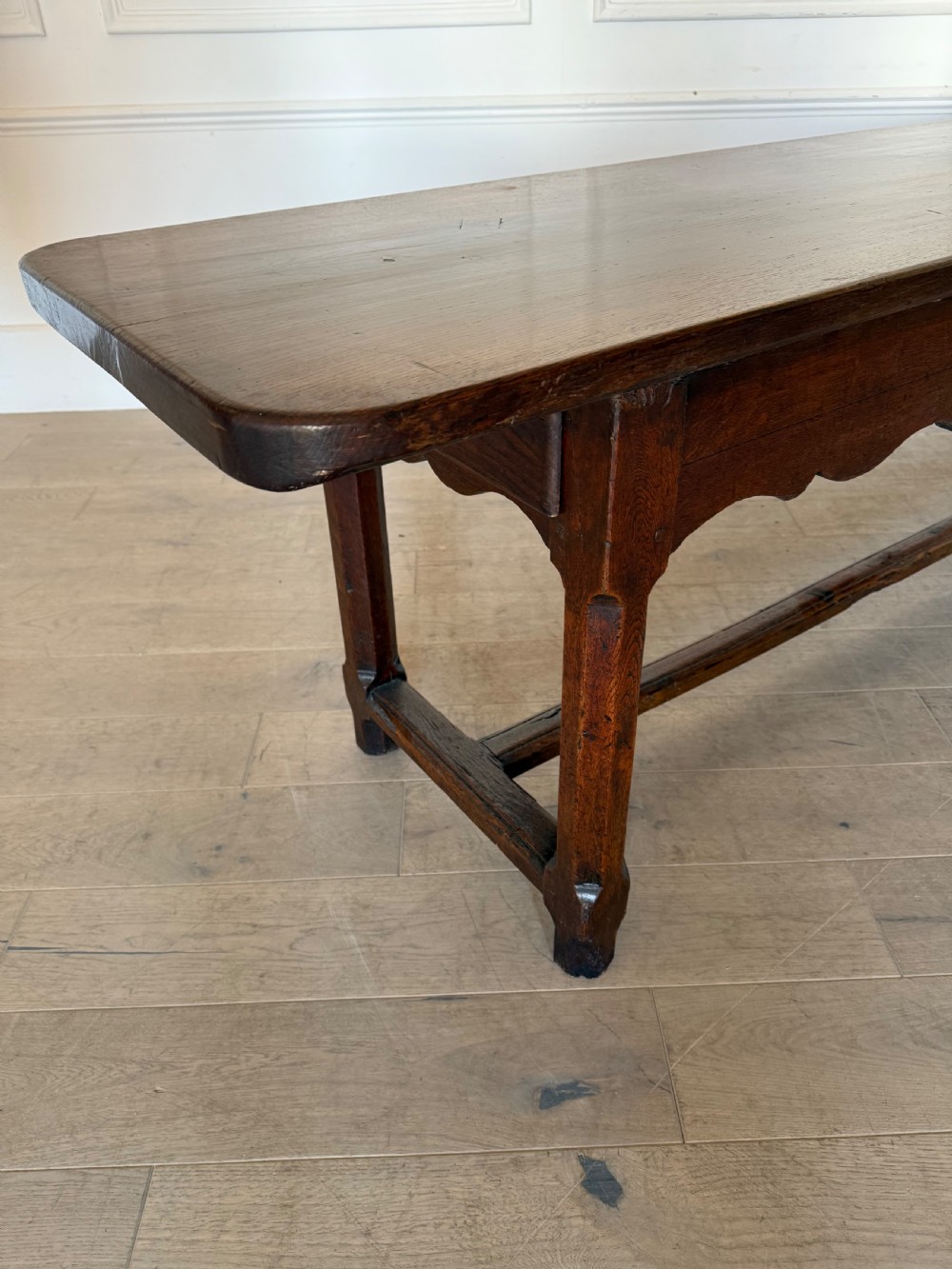 An eighteenth century oak console table with a rectangular plank top and a shaped frieze above plain stretcher-joined legs. View XVI