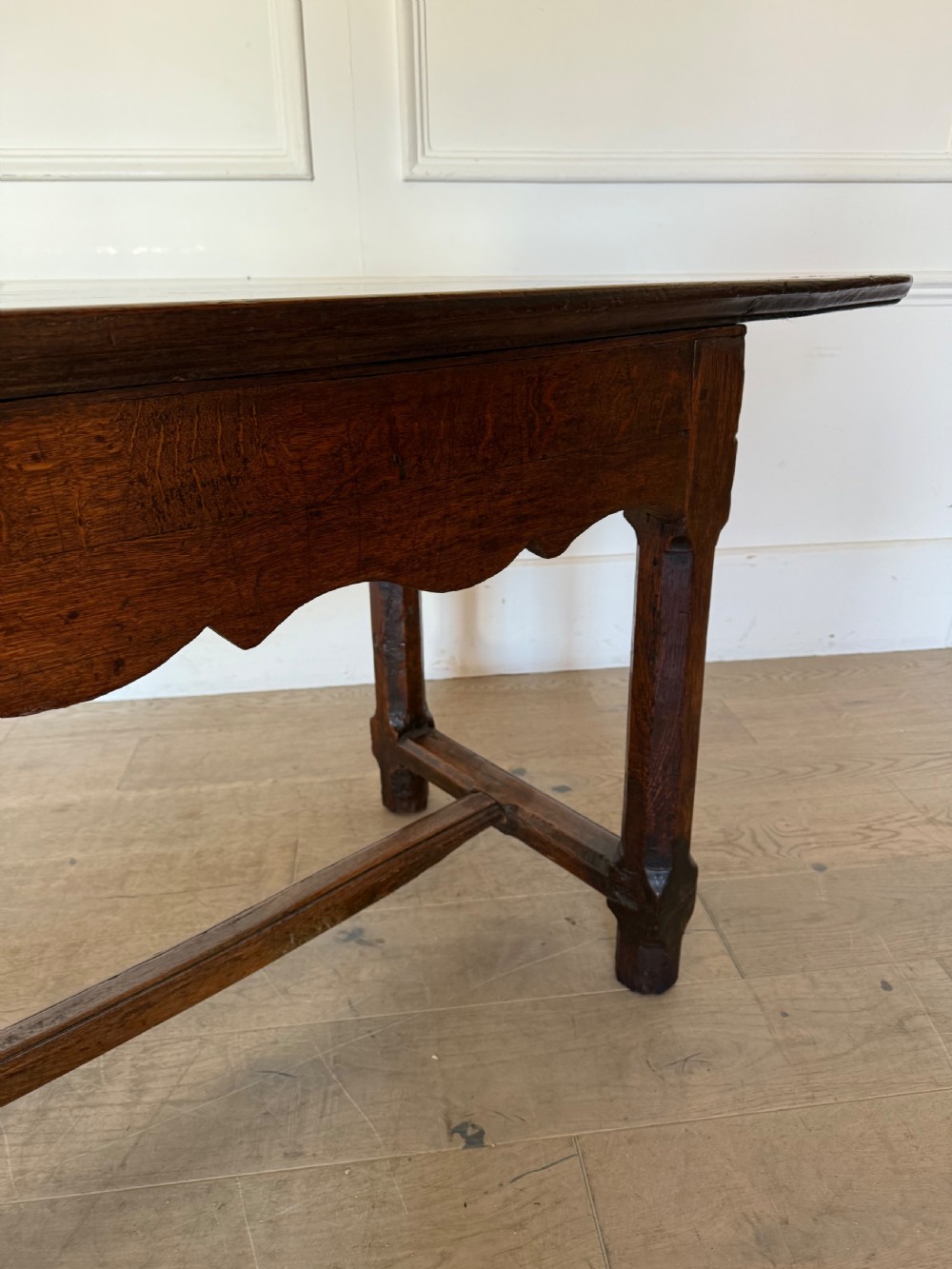 An eighteenth century oak console table with a rectangular plank top and a shaped frieze above plain stretcher-joined legs. View XX
