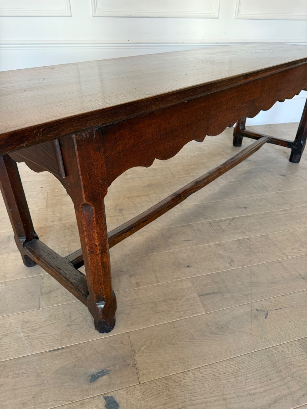 An eighteenth century oak console table with a rectangular plank top and a shaped frieze above plain stretcher-joined legs. View XXI