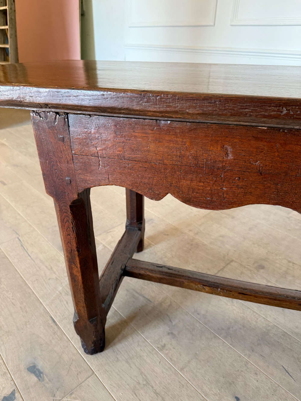 An eighteenth century oak console table with a rectangular plank top and a shaped frieze above plain stretcher-joined legs. View XXII