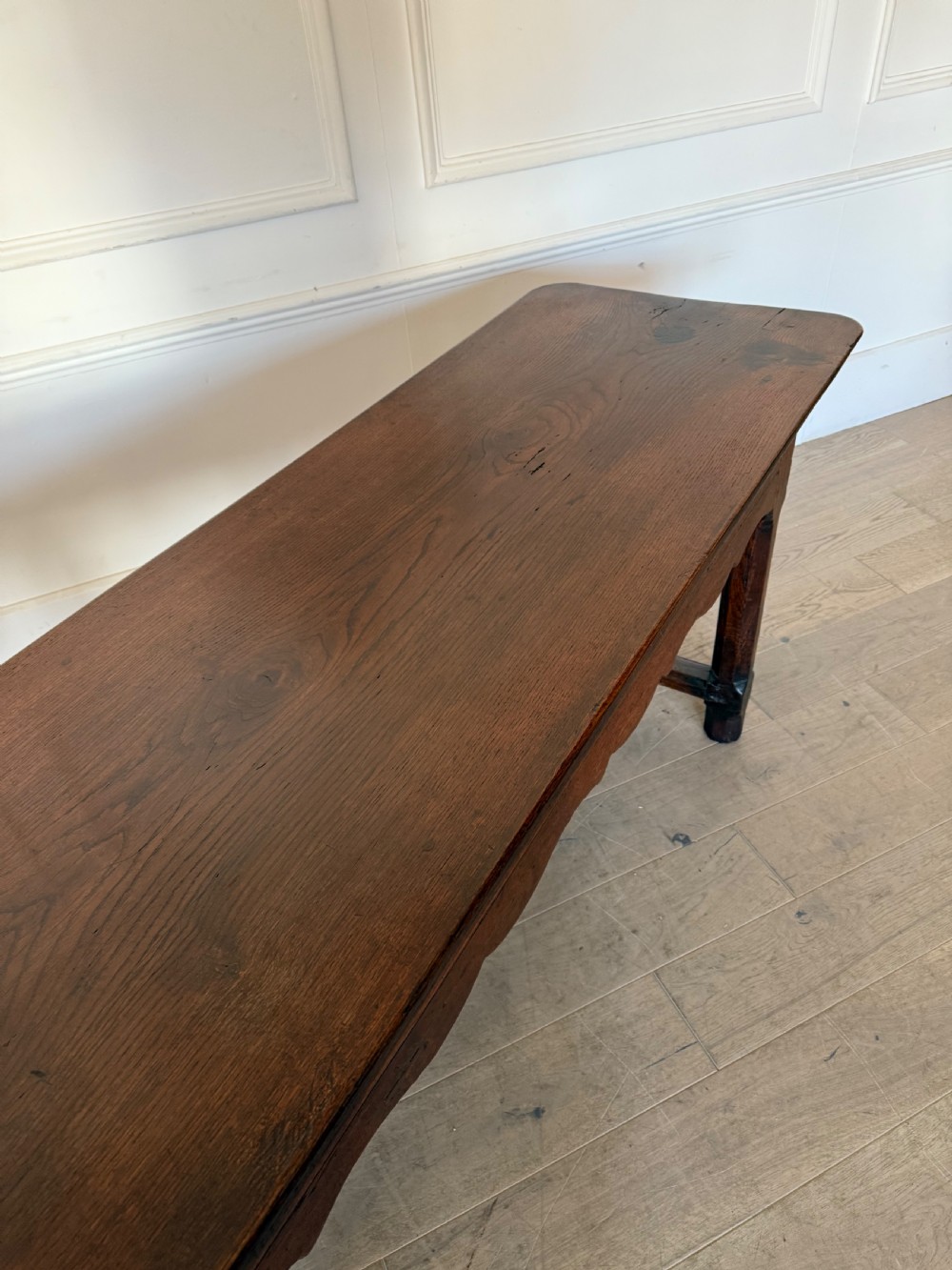 An eighteenth century oak console table with a rectangular plank top and a shaped frieze above plain stretcher-joined legs. View XXIII