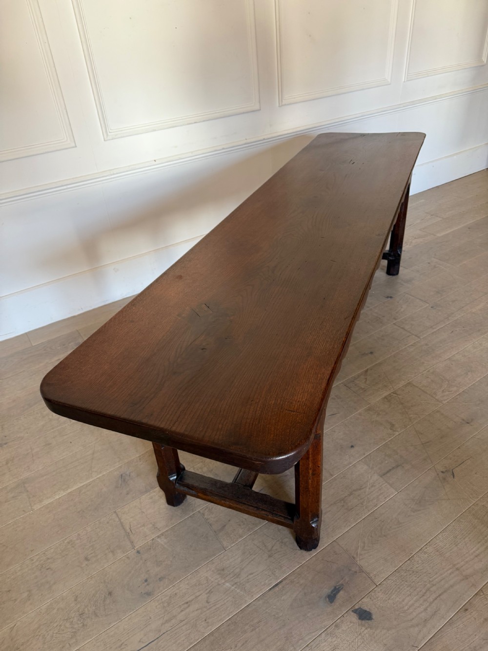 An eighteenth century oak console table with a rectangular plank top and a shaped frieze above plain stretcher-joined legs. View XXIV