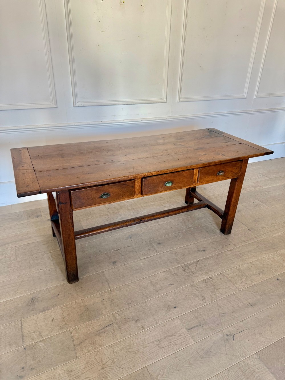 A rectangular 19th-century walnut drapers table featuring a plank top, three drawers with metal drop handles, and an H-stretcher base.