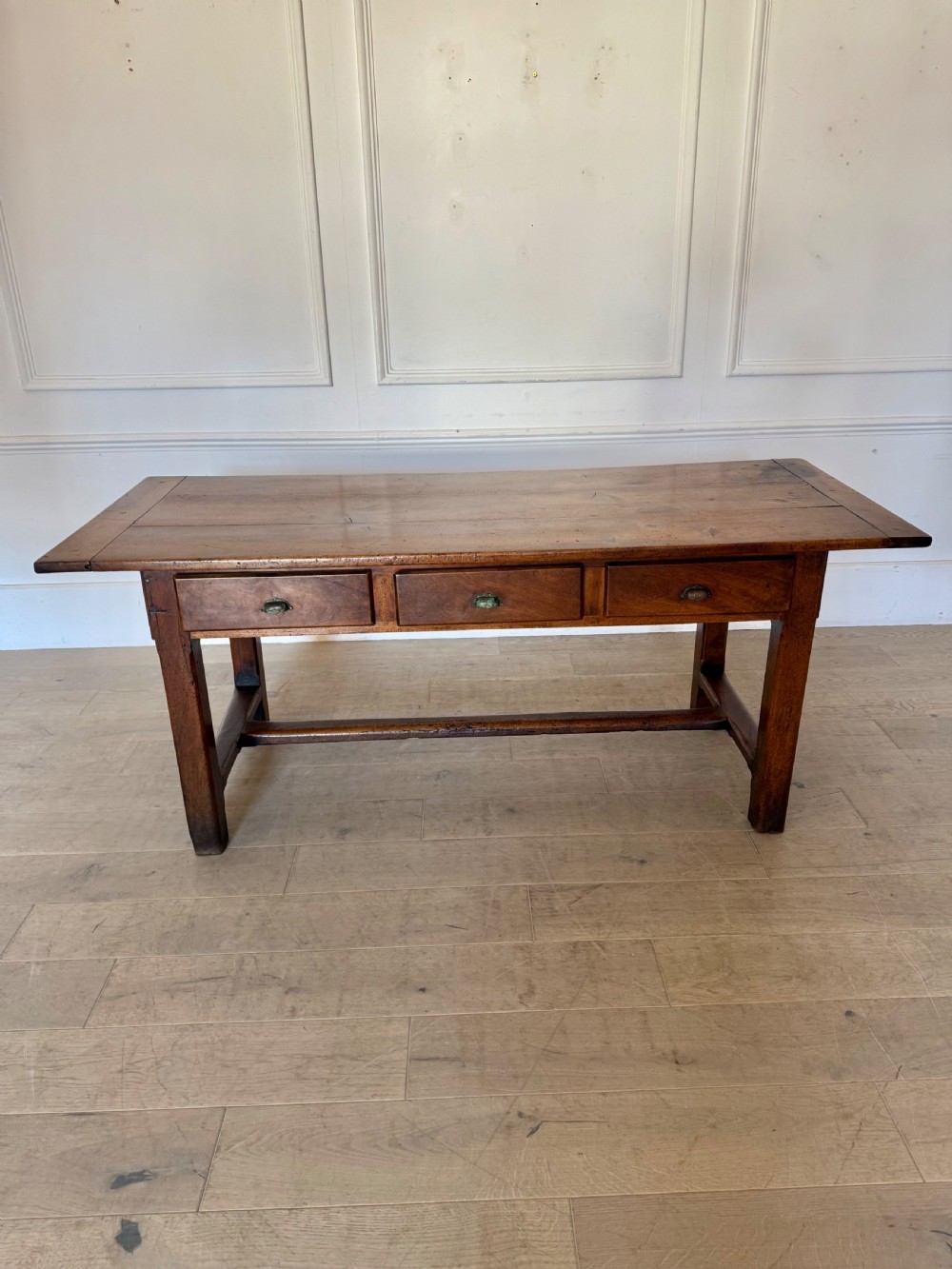 A rectangular 19th-century walnut drapers table featuring a plank top, three drawers with metal drop handles, and an H-stretcher base. View V