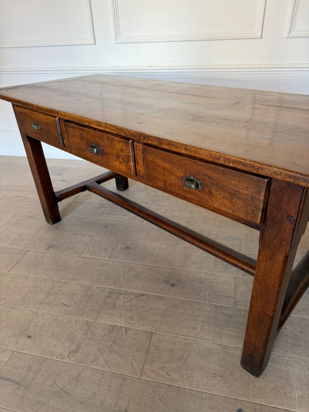 A rectangular 19th-century walnut drapers table featuring a plank top, three drawers with metal drop handles, and an H-stretcher base. View XVII