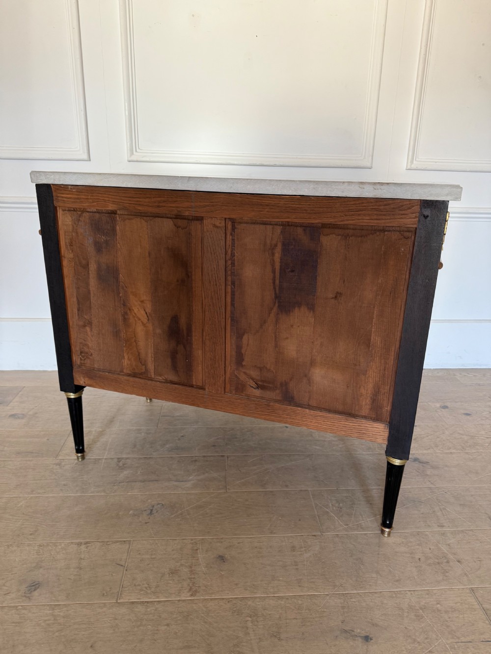 An ebonised commode chest of drawers featuring a grey marble top, brass ring handles, and gilt metal mounts. View XIII