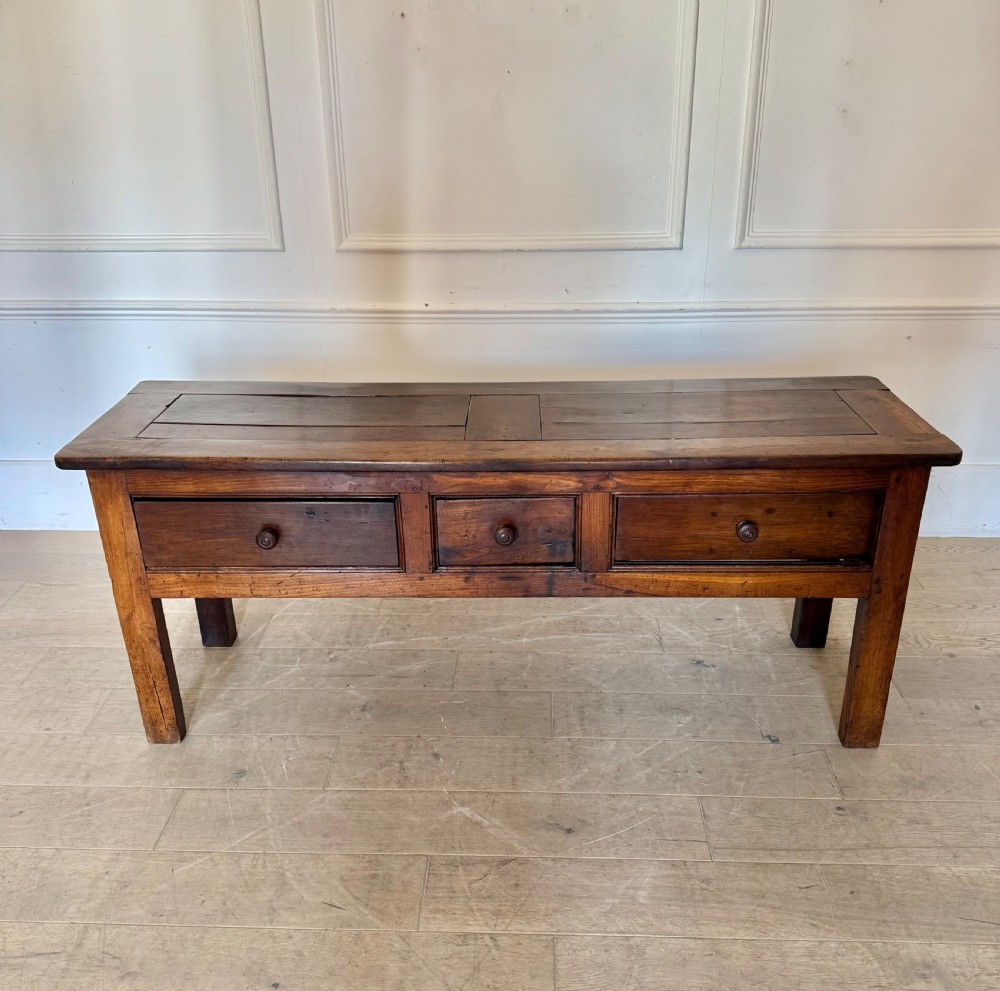 A rectangular early 19th-century chestnut dresser base featuring three drawers with turned wooden knobs and straight legs.
