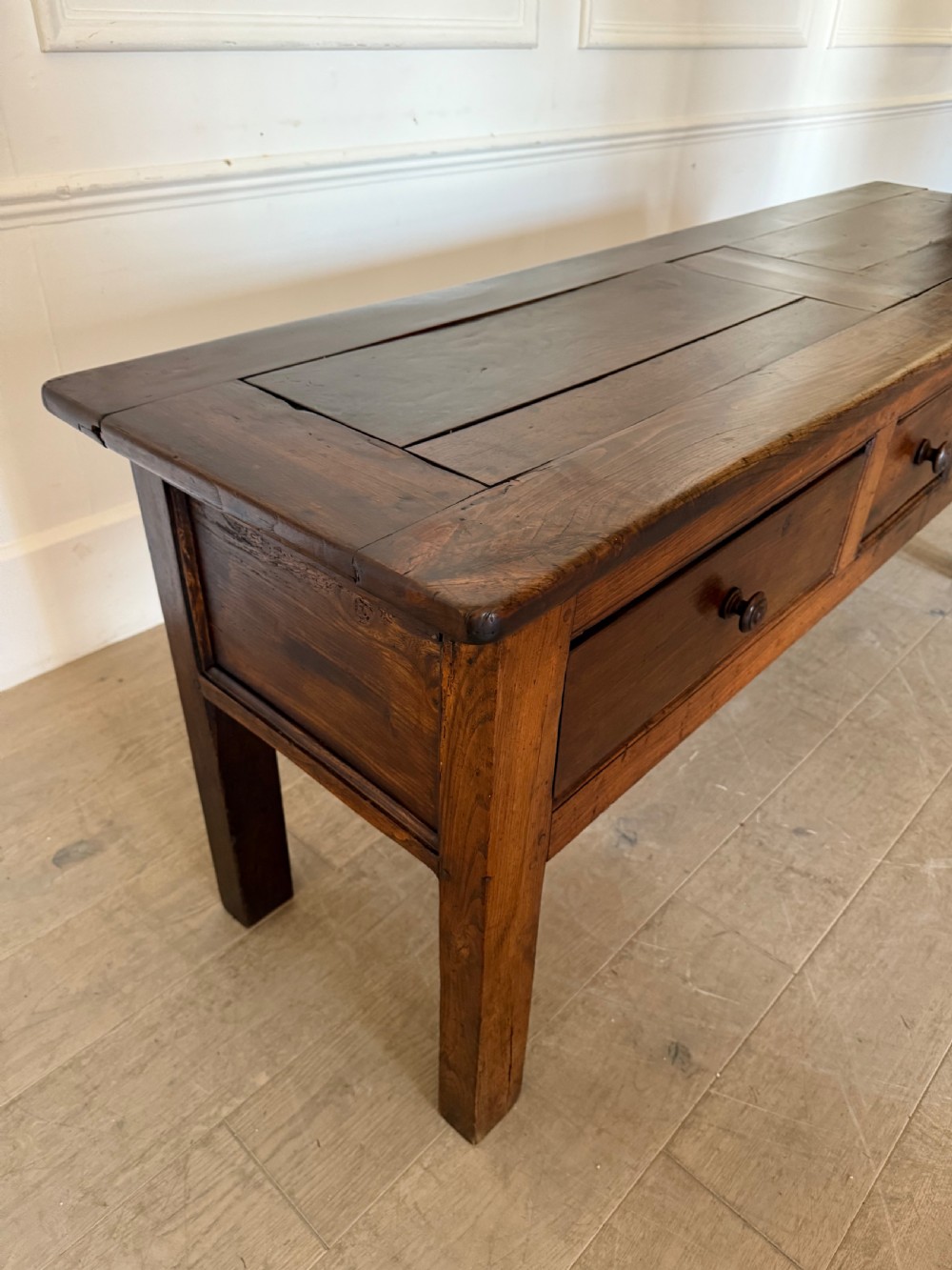 A rectangular early 19th-century chestnut dresser base featuring three drawers with turned wooden knobs and straight legs. View V