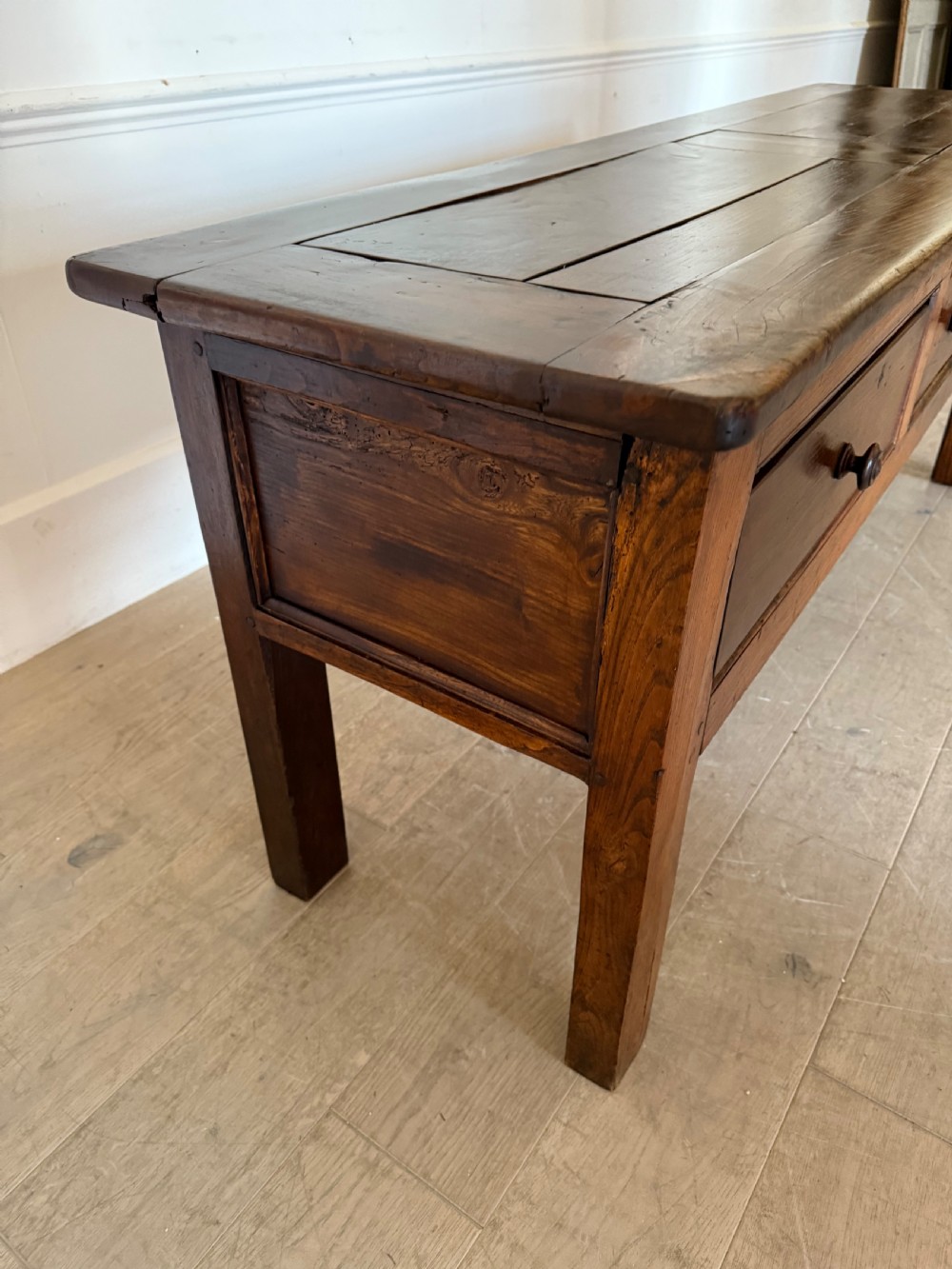 A rectangular early 19th-century chestnut dresser base featuring three drawers with turned wooden knobs and straight legs. View VI