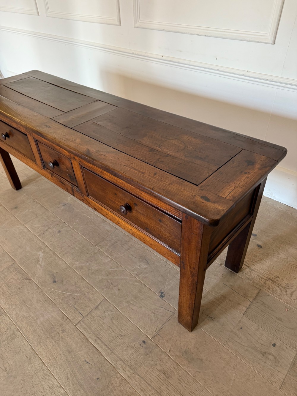 A rectangular early 19th-century chestnut dresser base featuring three drawers with turned wooden knobs and straight legs. View IX