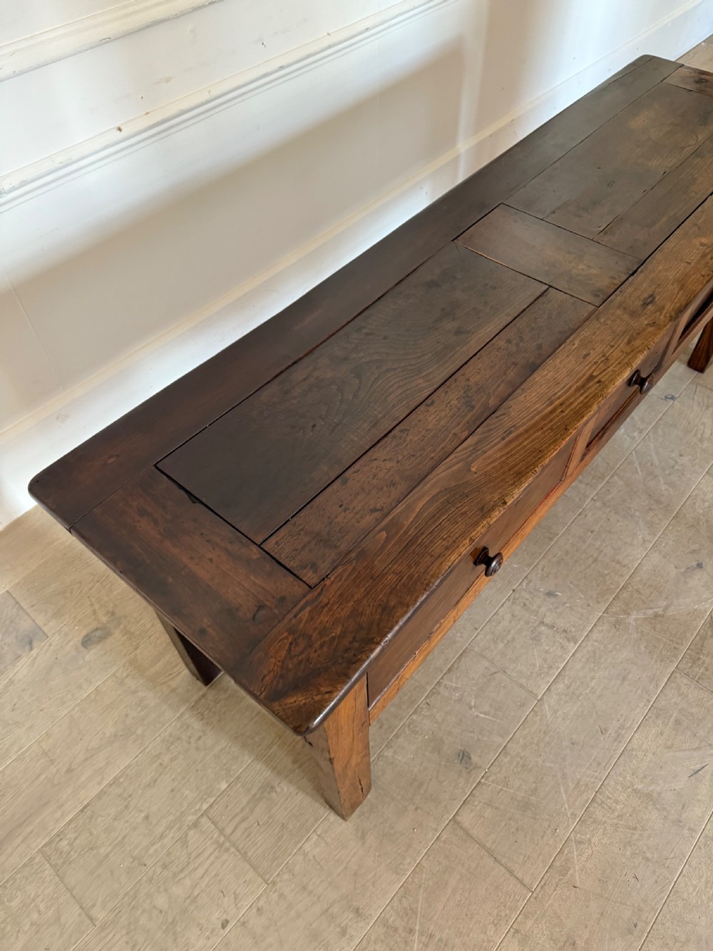 A rectangular early 19th-century chestnut dresser base featuring three drawers with turned wooden knobs and straight legs. View X