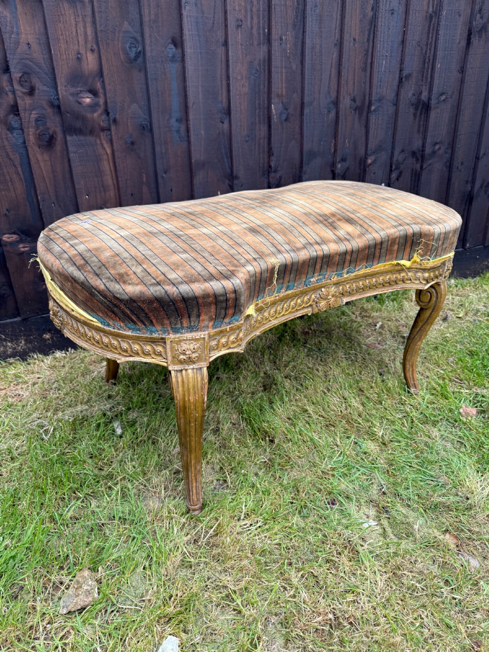 A Louis XVI style kidney-shaped stool featuring a carved giltwood frame with fluted legs and a striped fabric seat.
