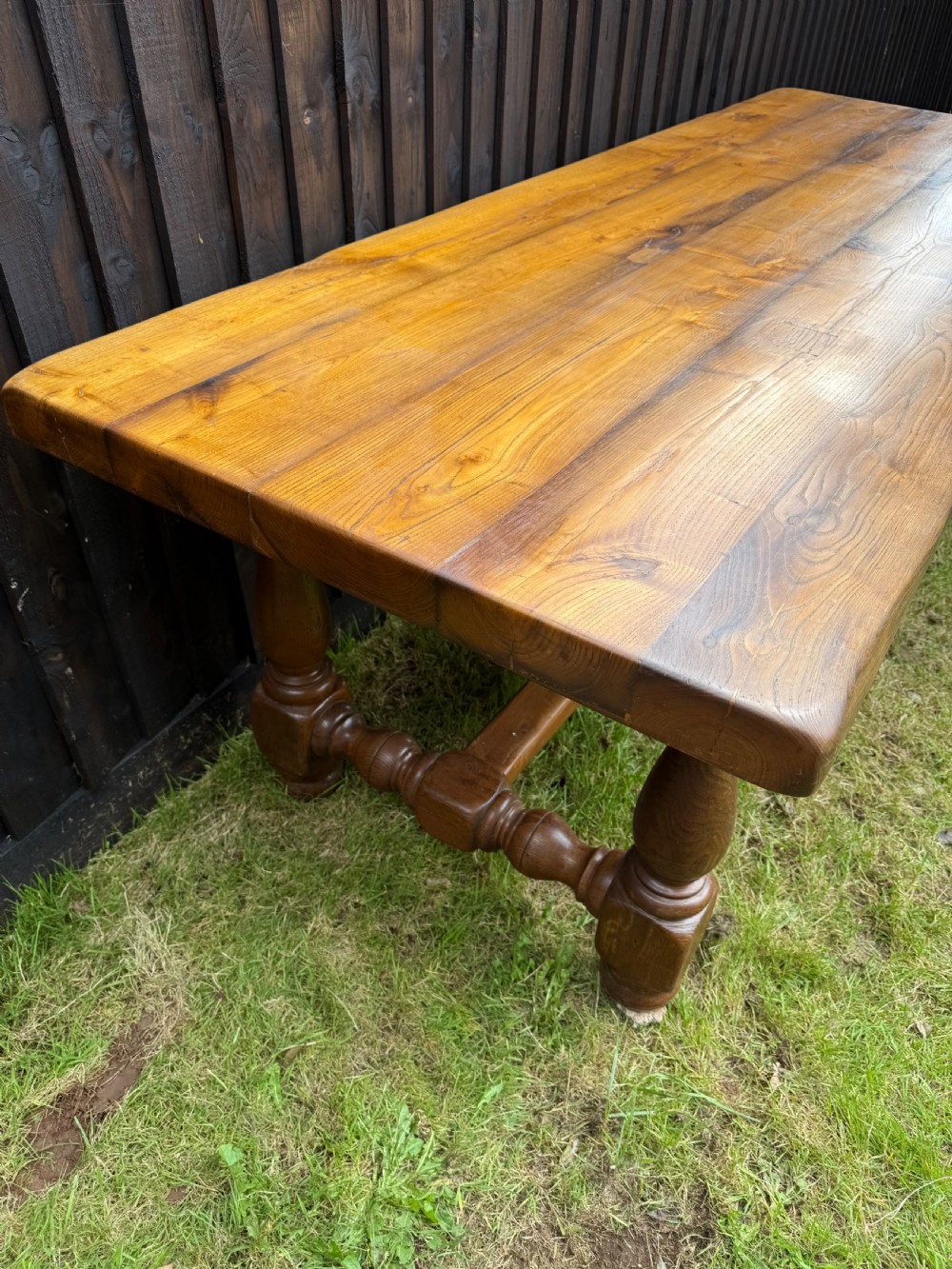 A large solid oak refectory dining table featuring a thick plank top, turned legs, and a low central stretcher base. View X