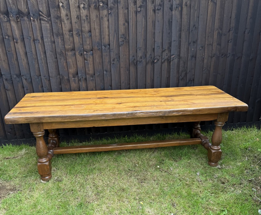 A large solid oak refectory dining table featuring a thick plank top, turned legs, and a low central stretcher base.