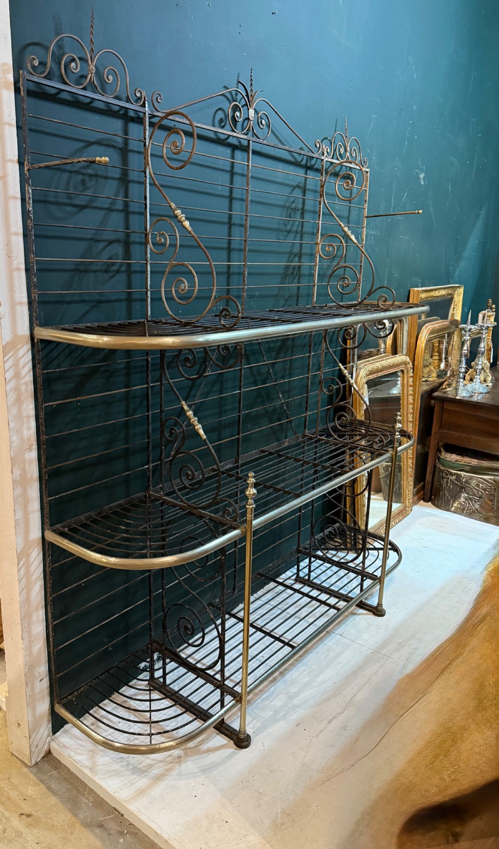 An antique French wrought iron and brass boulangerie rack featuring tier wire shelving and scrollwork cresting.