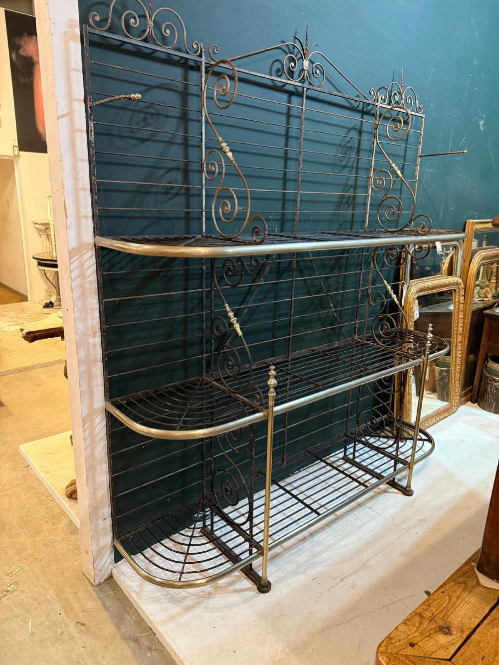 An antique French wrought iron and brass boulangerie rack featuring tier wire shelving and scrollwork cresting. View II