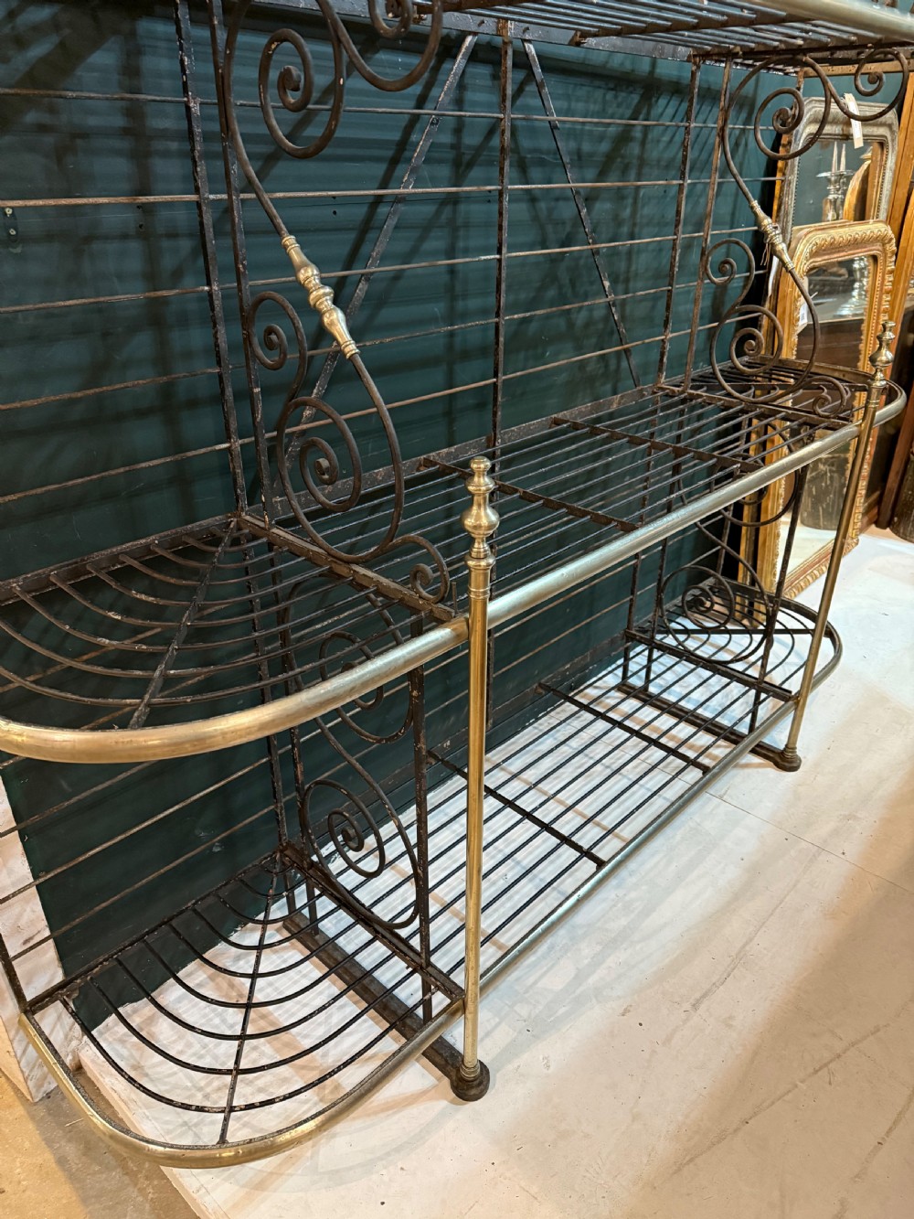 An antique French wrought iron and brass boulangerie rack featuring tier wire shelving and scrollwork cresting. View XIV