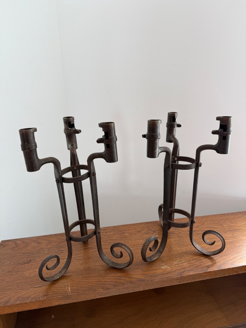 A pair of dark patinated metal three-light candelabras constructed from re-purposed military bayonet parts and scrollwork legs.